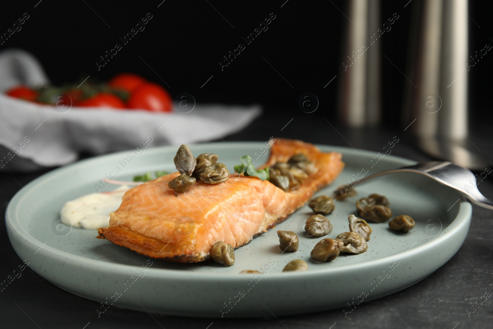 Photo of Delicious salmon with capers and sauce served on dark table, closeup