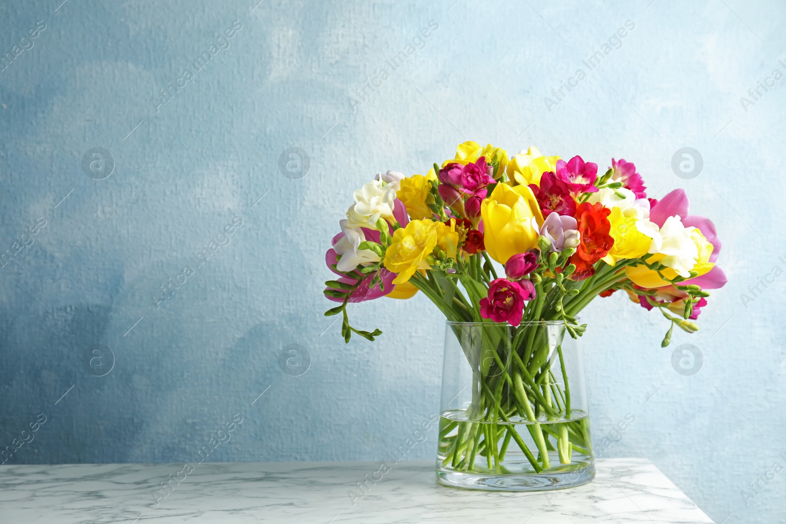 Photo of Bouquet of spring freesia flowers in vase on table against color background. Space for text