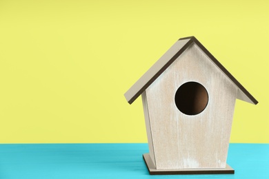 Beautiful bird house on light blue wooden table against yellow background, space for text