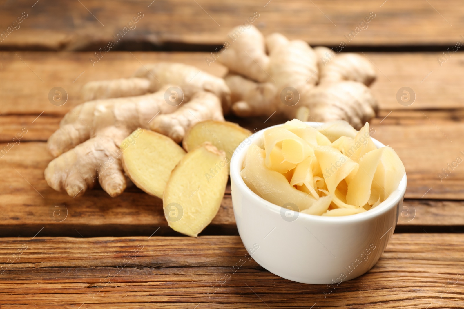 Photo of Spicy pickled ginger and root on wooden table, space for text