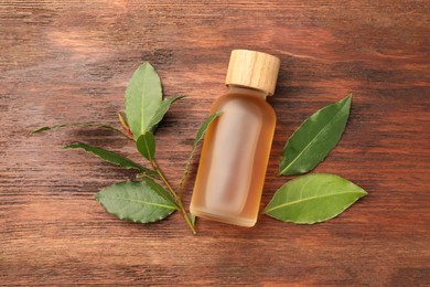 Bottle of bay essential oil and fresh leaves on wooden table, flat lay
