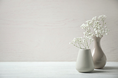 Photo of Gypsophila flowers in vases on table against light background. Space for text