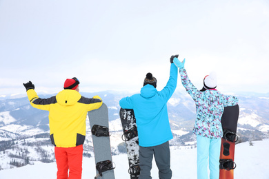 Friends with snowboards at mountain resort, back view. Winter vacation
