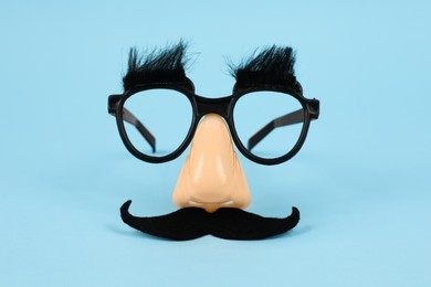 Photo of Funny mask with fake mustache, nose and glasses on light blue background