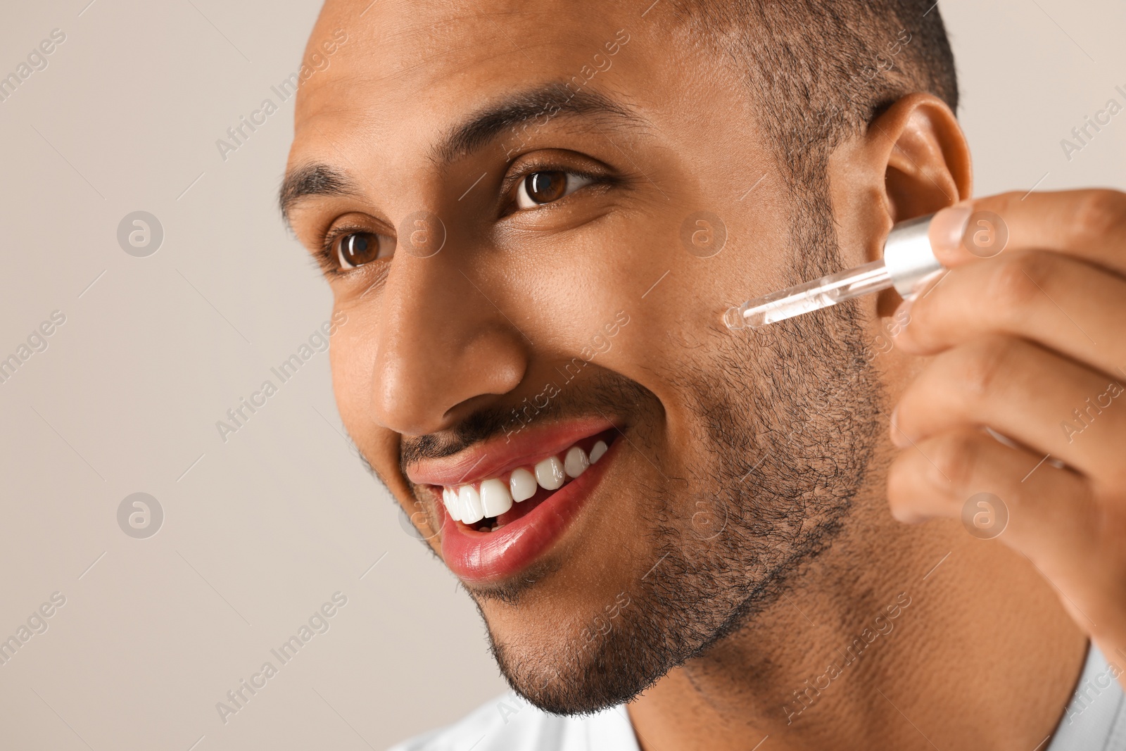 Photo of Handsome man applying cosmetic serum onto face on light grey background, closeup