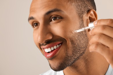 Photo of Handsome man applying cosmetic serum onto face on light grey background, closeup