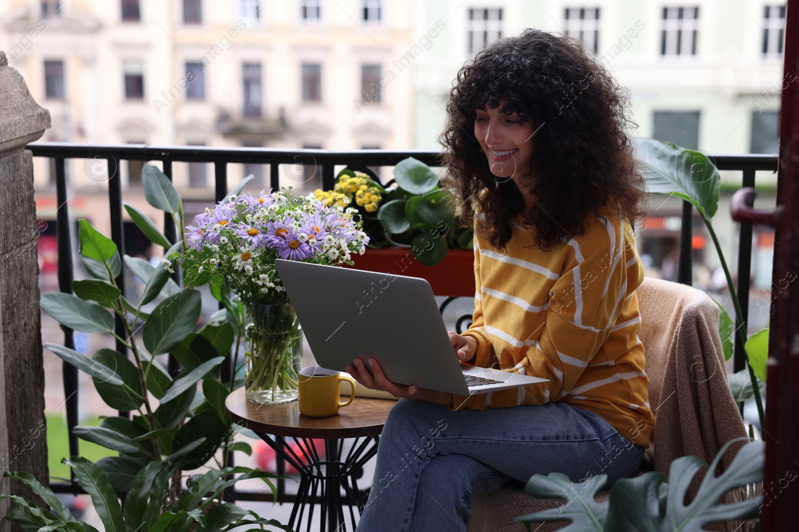 Photo of Beautiful young woman using laptop on balcony with green houseplants
