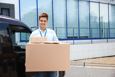 Photo of Young courier holding parcels near delivery car outdoors. Space for text