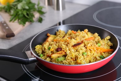 Tasty rice with meat and vegetables in frying pan on induction stove, closeup