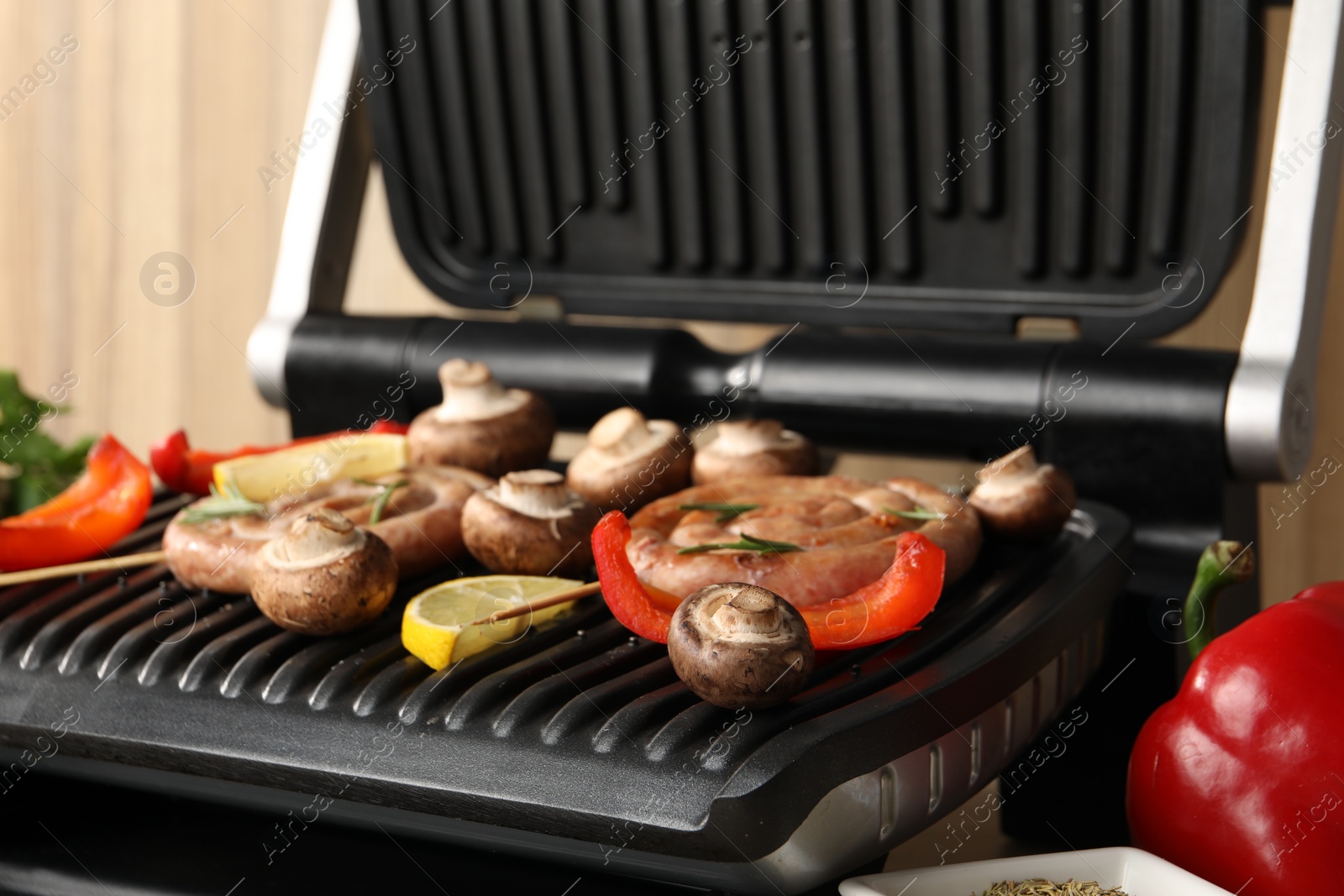 Photo of Electric grill with homemade sausages, mushrooms and bell pepper on table, closeup