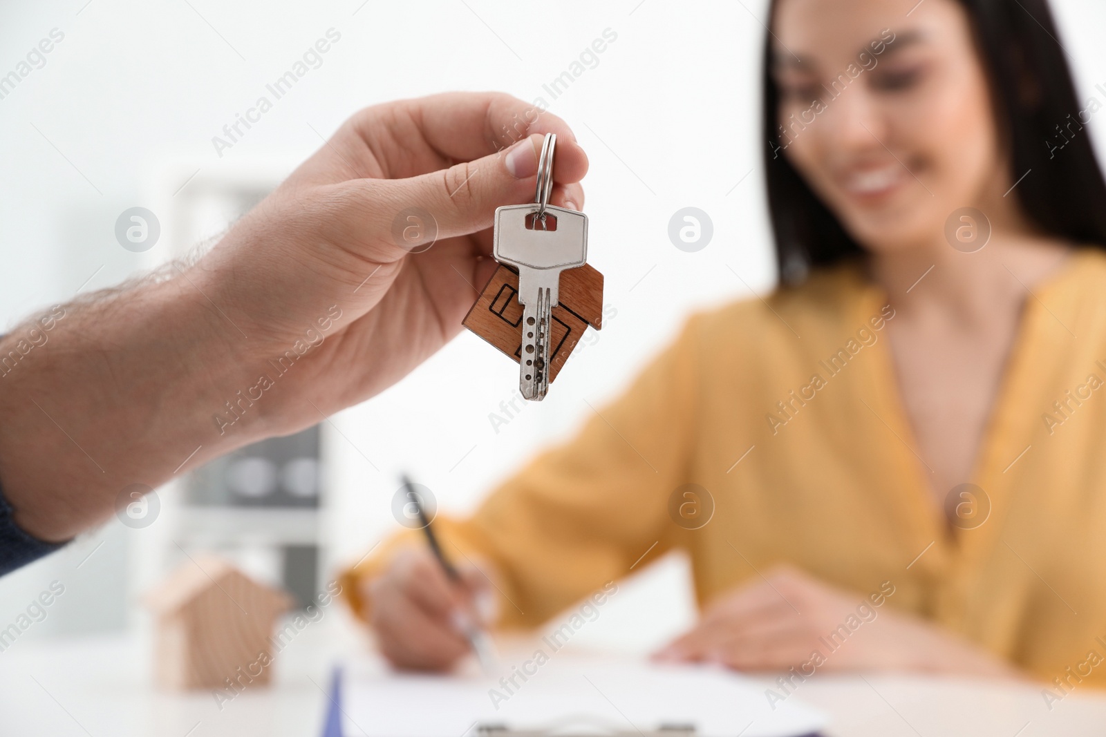 Photo of Happy young woman signing purchase contract in office. Real estate agent holding new house key, closeup