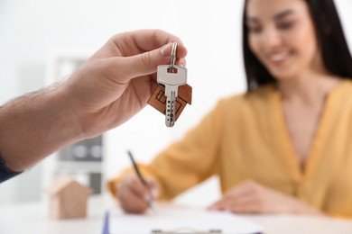 Photo of Happy young woman signing purchase contract in office. Real estate agent holding new house key, closeup