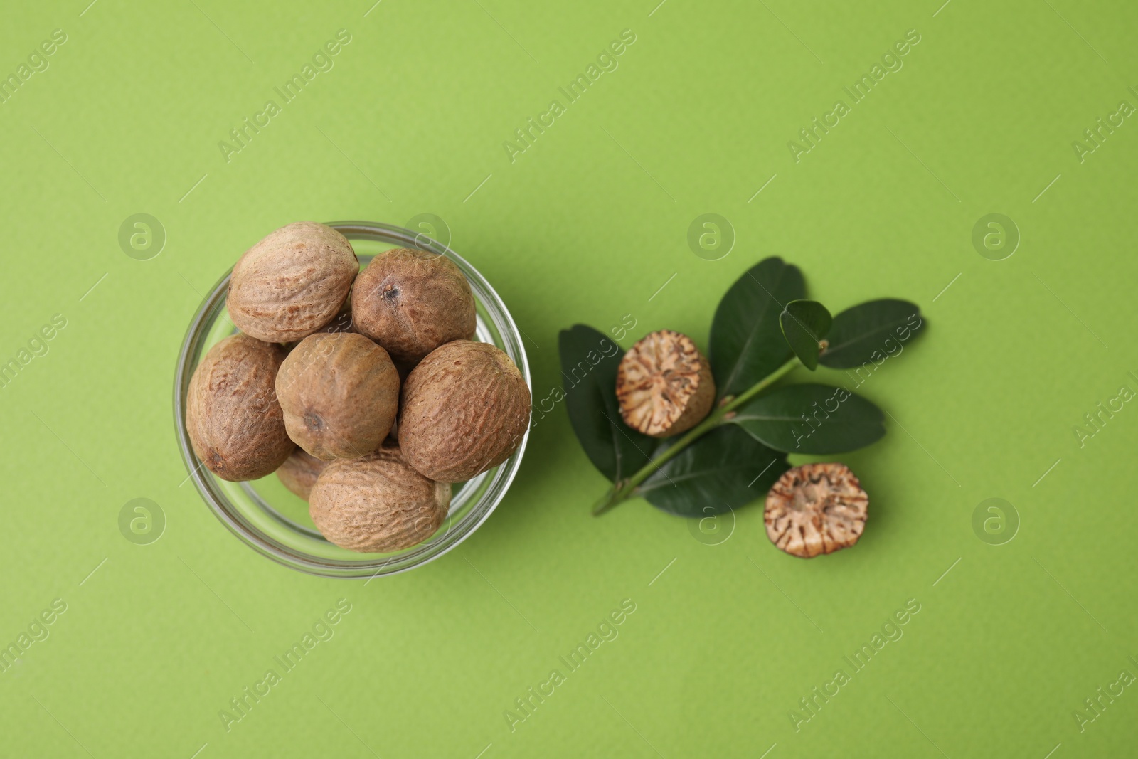 Photo of Nutmegs in bowl and branch on light green background, flat lay