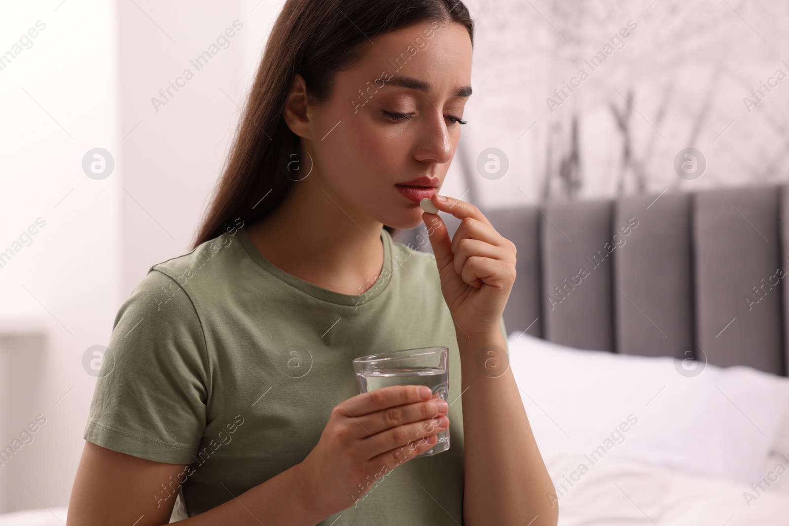 Photo of Depressed woman with glass of water taking antidepressant pill on bed indoors, space for text