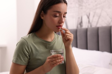 Photo of Depressed woman with glass of water taking antidepressant pill on bed indoors, space for text