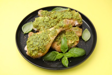 Delicious fried chicken drumsticks with pesto sauce and basil on yellow table, closeup