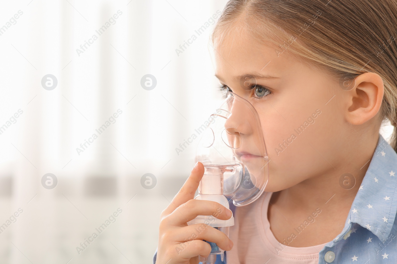 Photo of Sick little girl using nebulizer for inhalation indoors