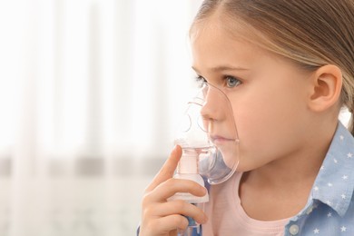 Photo of Sick little girl using nebulizer for inhalation indoors
