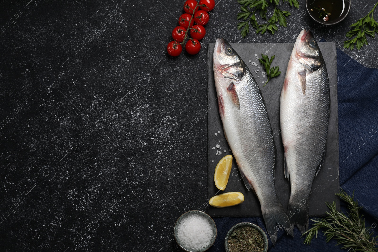 Photo of Fresh raw sea bass fish and ingredients on black table, flat lay. Space for text