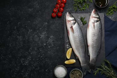Photo of Fresh raw sea bass fish and ingredients on black table, flat lay. Space for text