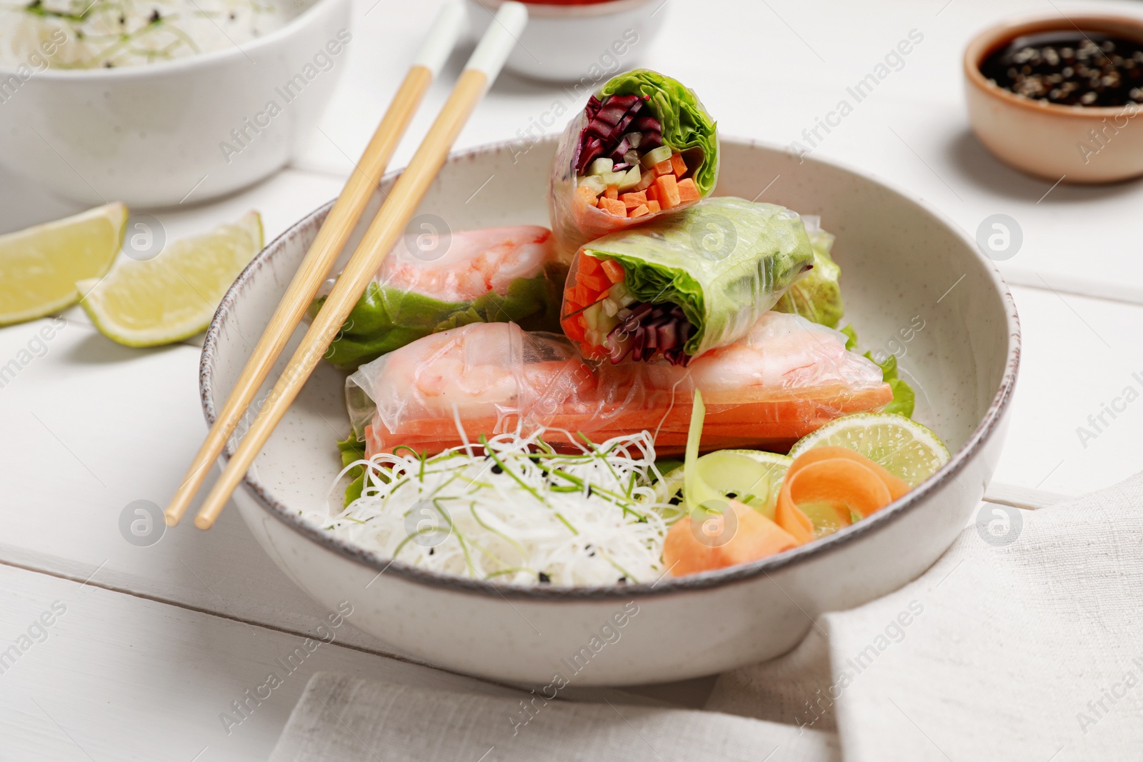 Photo of Delicious spring rolls wrapped in rice paper served on white wooden table, closeup