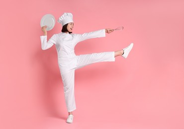 Photo of Happy confectioner with plate and whisk on pink background