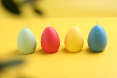 Photo of Colorful egg shaped candles on yellow background. Easter decor
