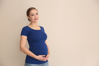Young pregnant woman on beige background. Space for text