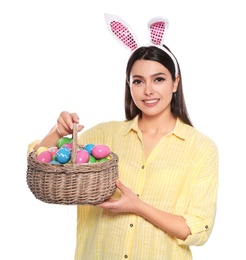 Photo of Beautiful woman in bunny ears headband holding basket with Easter eggs on white background