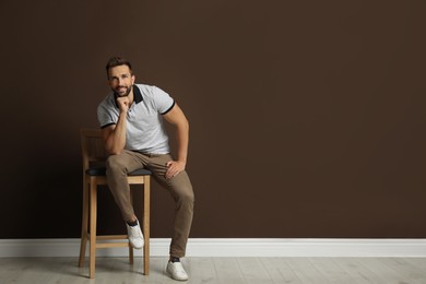 Photo of Handsome man sitting on stool near brown wall. Space for text
