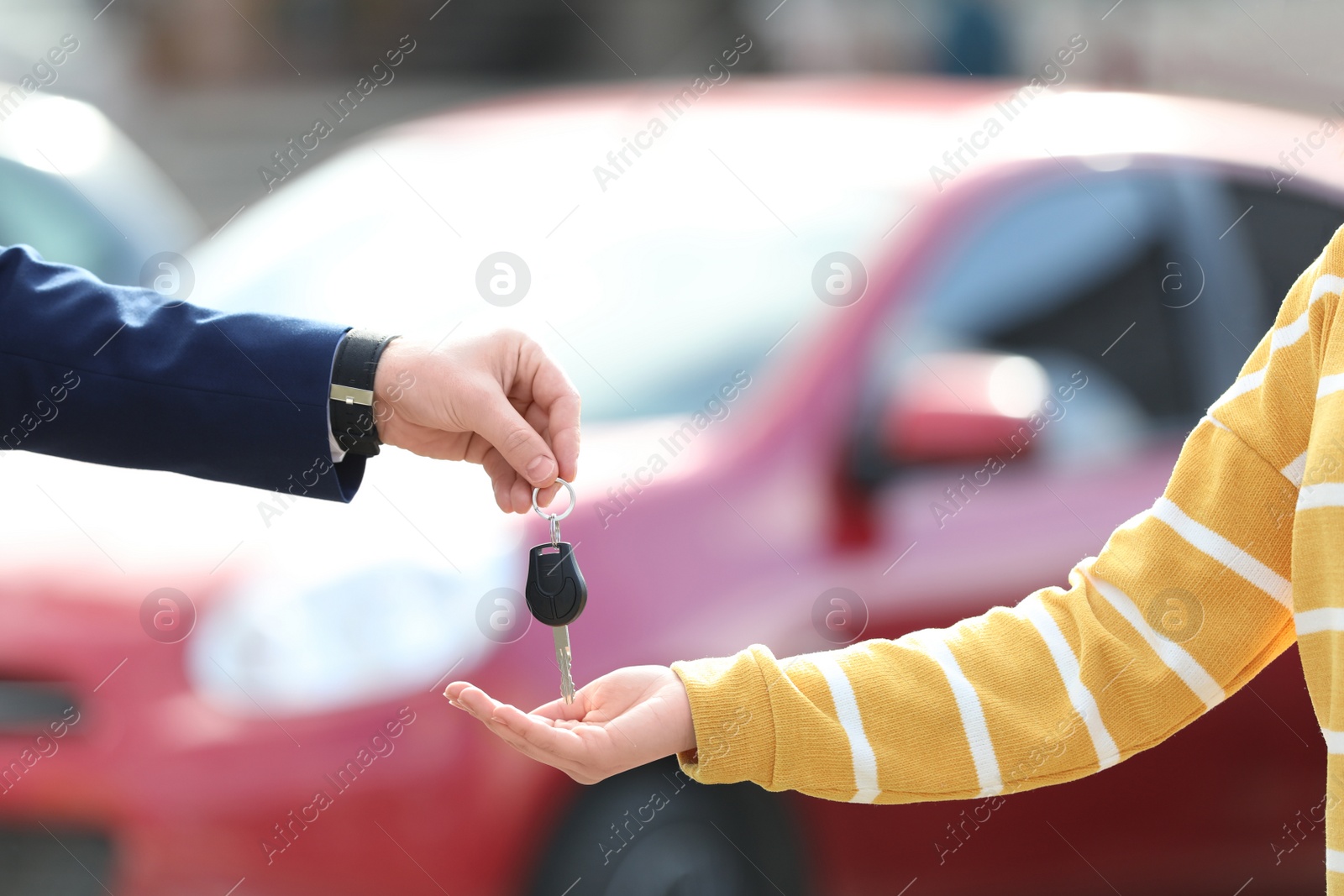 Photo of Salesman giving key to customer in modern auto dealership, closeup. Buying new car