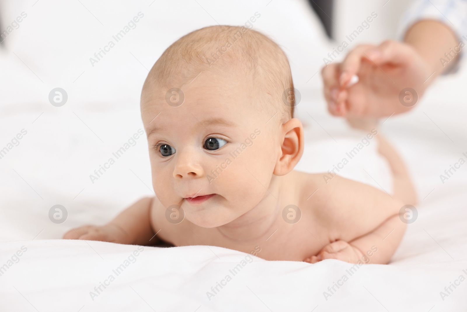 Photo of Woman applying body cream onto baby`s skin on bed, closeup