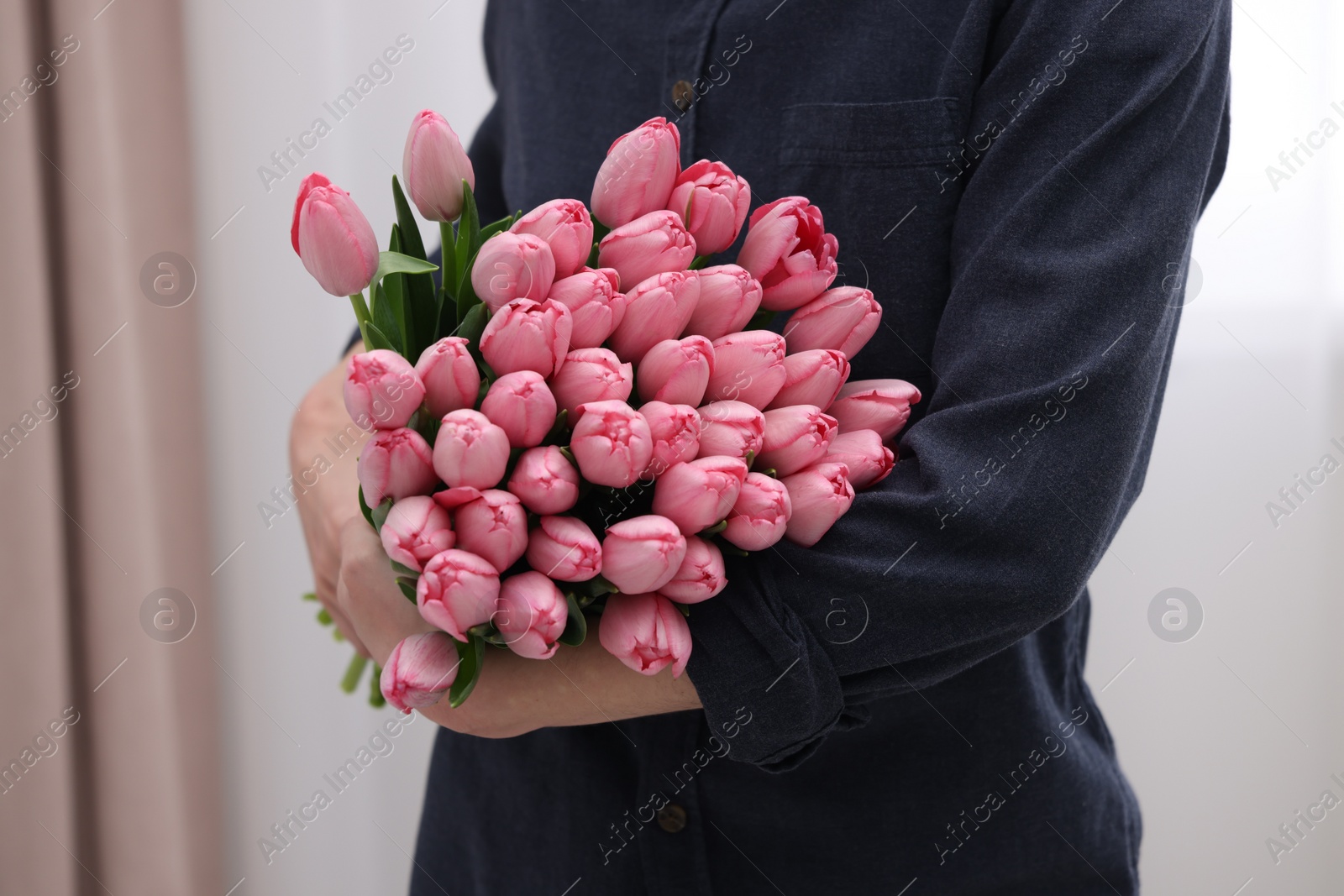 Photo of Woman holding bouquet of pink tulips indoors, closeup