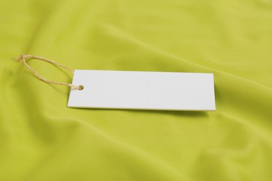 Blank white tag on green fabric, closeup. Space for text