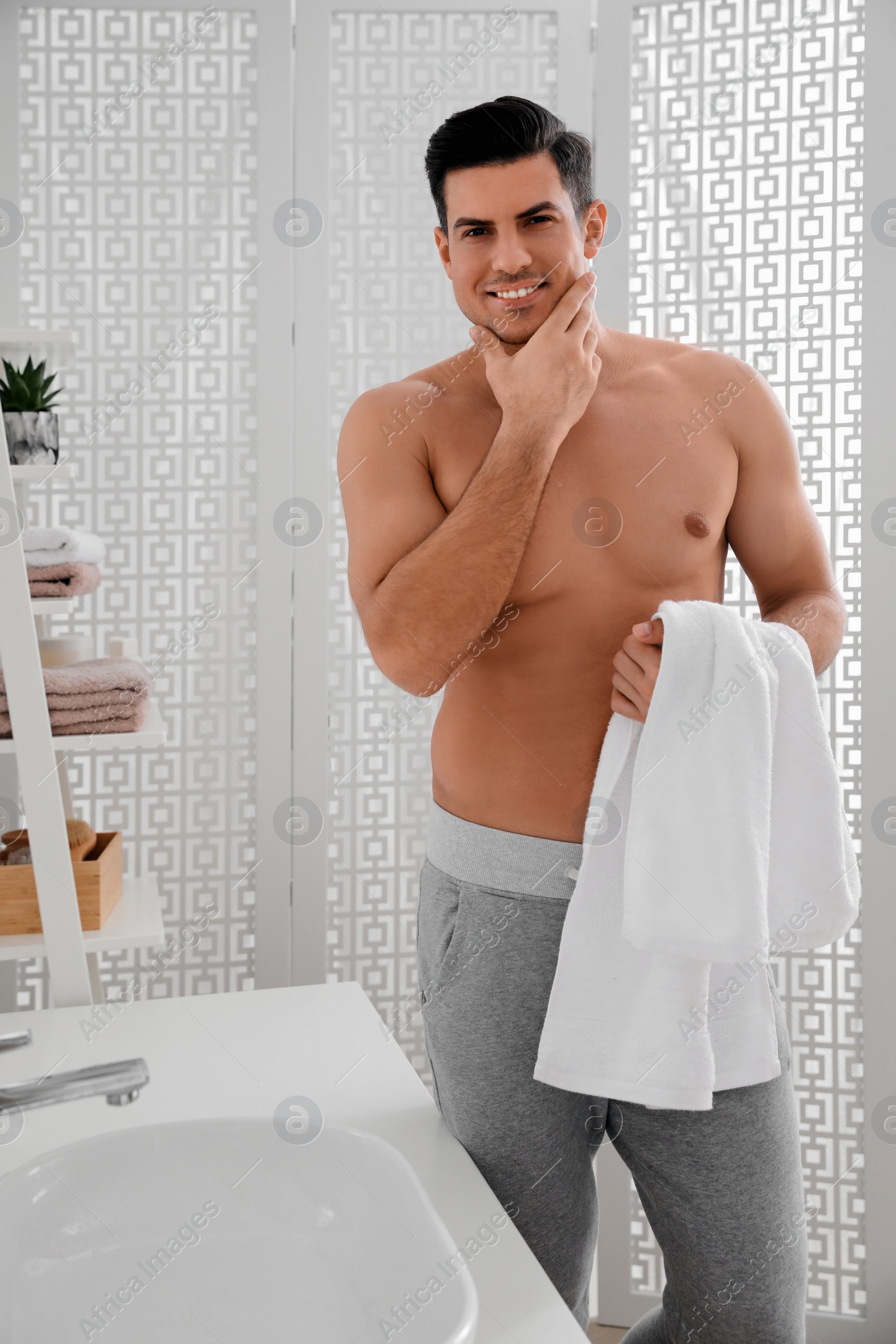 Photo of Handsome man touching his smooth face in bathroom after shaving
