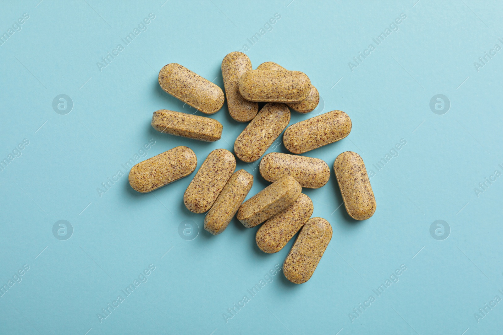 Photo of Dietary supplement pills on light blue background, flat lay