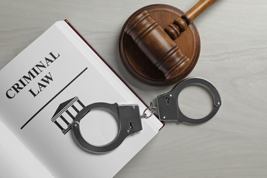 Judge's gavel, handcuffs and Criminal law book on white wooden background, flat lay