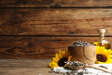 Photo of Organic sunflower seeds and flowers on wooden table. Space for text