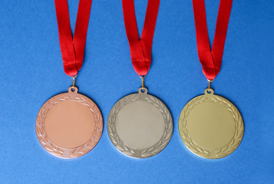 Gold, silver and bronze medals on blue background, flat lay. Space for design