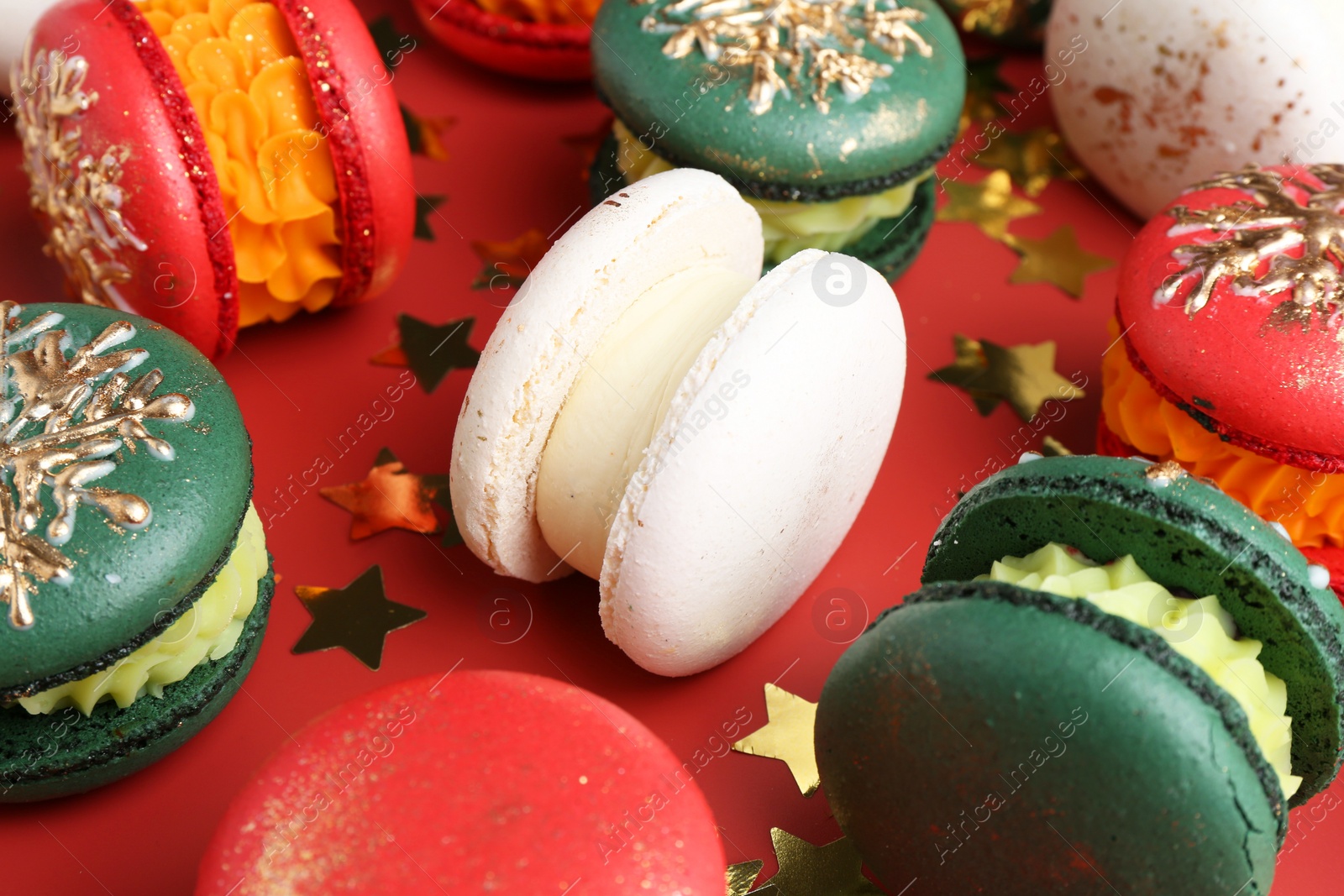 Photo of Beautifully decorated Christmas macarons and confetti on red background, closeup