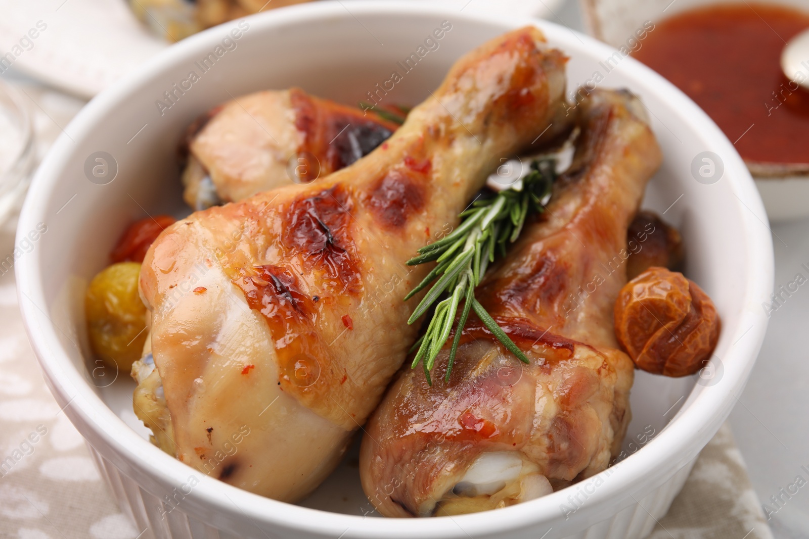 Photo of Delicious roasted chicken drumsticks with rosemary and tomatoes in bowl on table, closeup