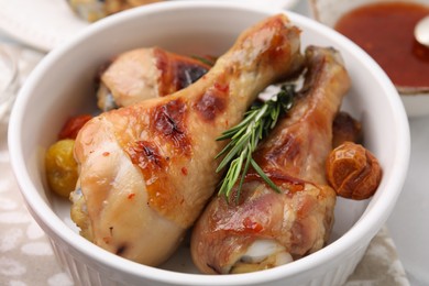 Delicious roasted chicken drumsticks with rosemary and tomatoes in bowl on table, closeup