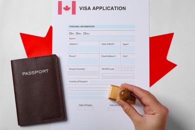 Photo of Immigration to Canada. Woman stamping visa application form on flag, top view