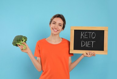 Photo of Woman holding blackboard with phrase Keto Diet and broccoli on light blue background