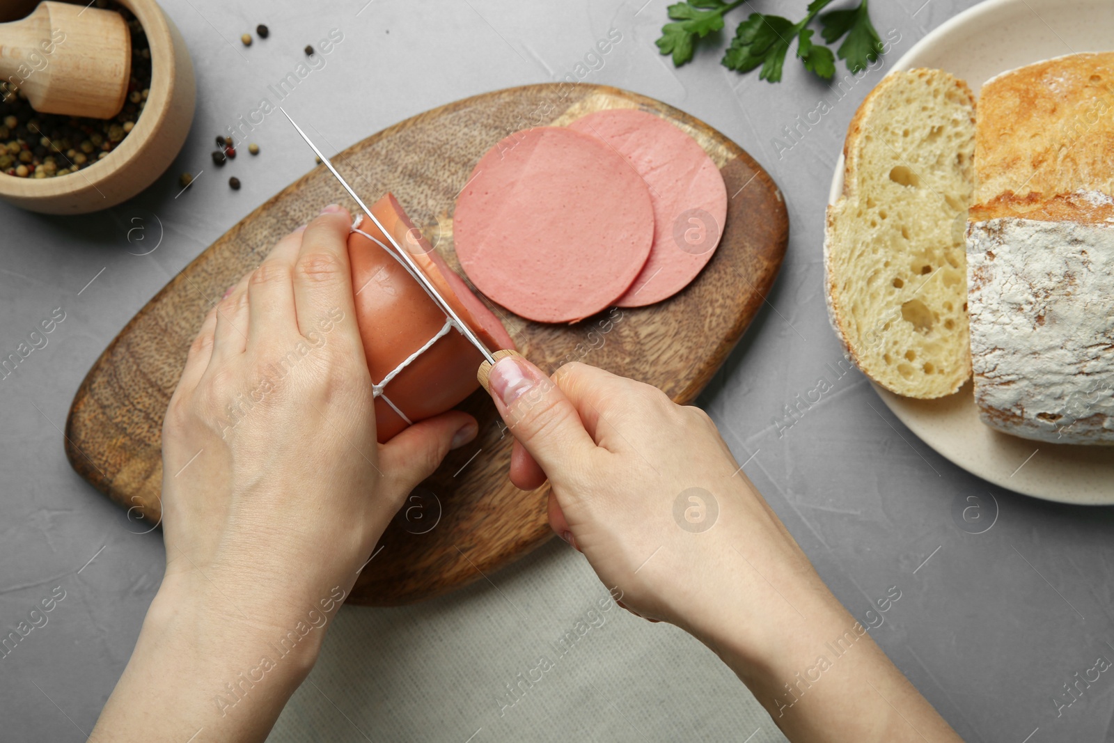 Photo of Woman cutting tasty boiled sausage at light grey textured table, top view