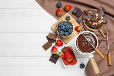 Fondue pot with chocolate, different berries and forks on white wooden table, flat lay. Space for text