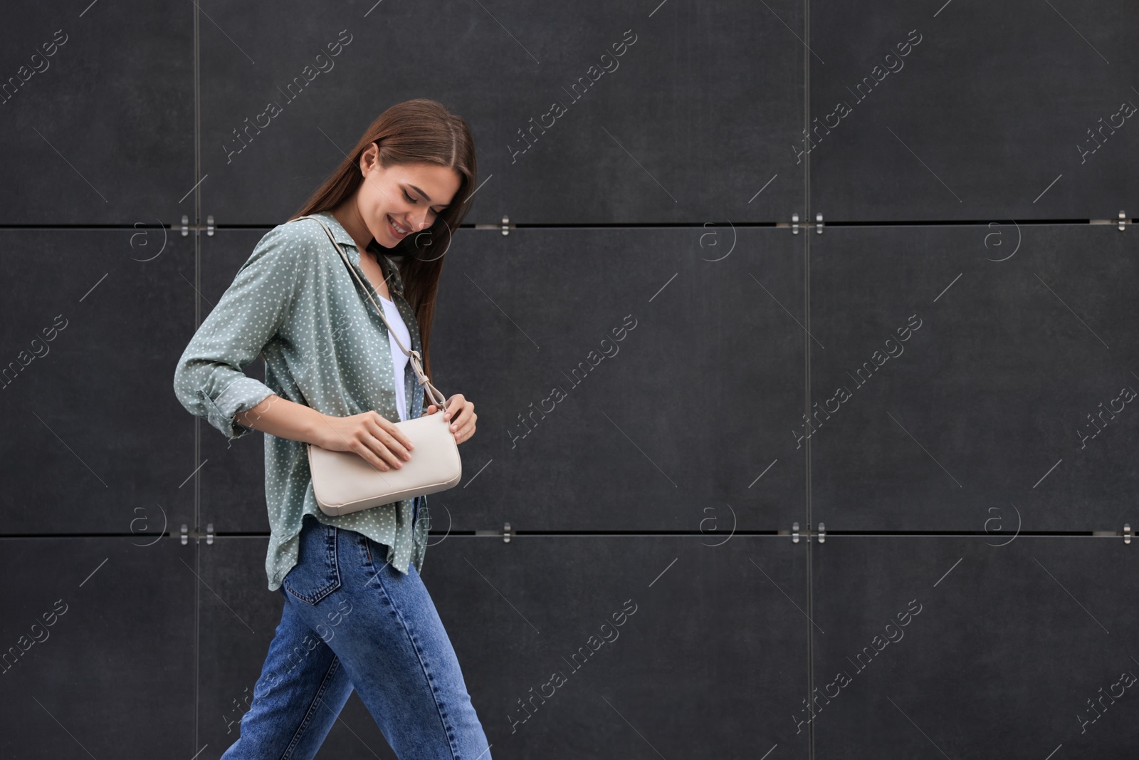 Photo of Young woman in casual clothes walking near grey wall outdoors, space for text