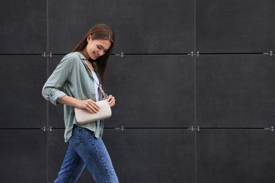 Photo of Young woman in casual clothes walking near grey wall outdoors, space for text