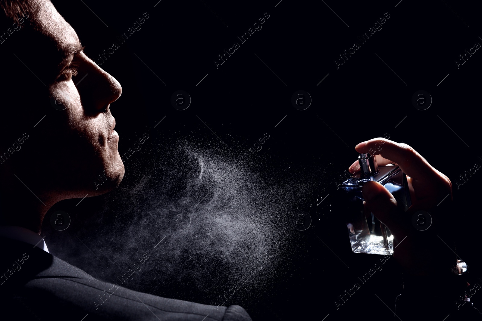 Photo of Man spraying luxury perfume on black background, closeup