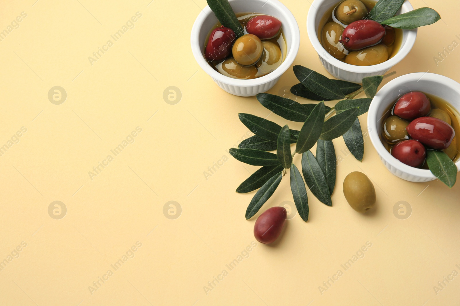 Photo of Bowls with different ripe olives and leaves on beige background. Space for text